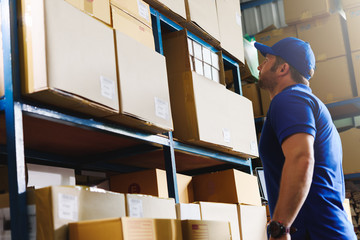 Portrait of delivery staff in blue uniform looking for particular box in warehouse