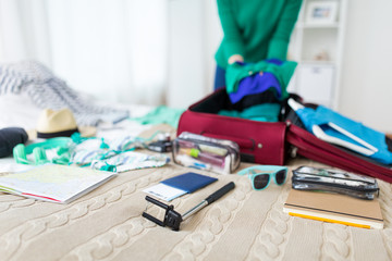 tourism, people and luggage concept - happy young woman packing travel bag at home or hotel room
