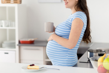 pregnancy, people and expectation concept - close up of pregnant woman with cup of tea at home kitchen