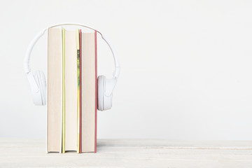Three books and hearphones on a wooden shelf against a white background. Reading concept and study metaphor with empty copy space for Editor's text.