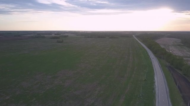 green unharvested fields and narrow forest belts surround wide highway after sunset pictorial bird eye view