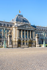 Three-quarter view of the colonnade and grid of the Royal Palace of Brussels, the official palace of the King and Queen of the Belgians in the historic center of Brussels, Belgium, under a blue sky.