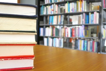 The old books with hard cover on the wooden table in the library. Selective focus with blurred bookshelves background. Education and book's day concept.