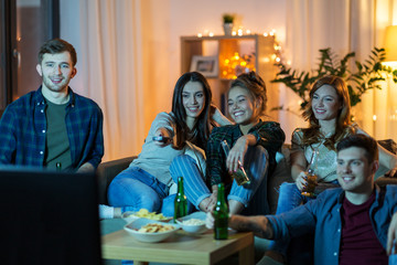 friendship, and leisure concept - happy friends with non-alcoholic drinks and snacks watching tv at home in evening