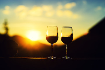 Two glasses of wine at sunset dramatic sky on mountain landscape background