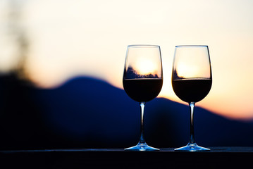 Two glasses of wine at sunset dramatic sky on mountain landscape background