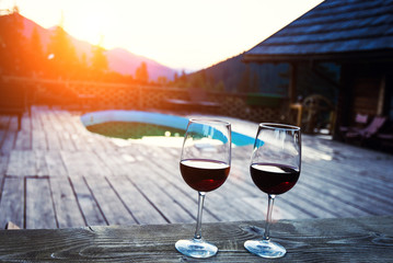 Two glasses of wine at sunset dramatic sky on mountain landscape background