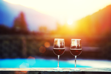 Two glasses of wine at sunset dramatic sky on mountain landscape background