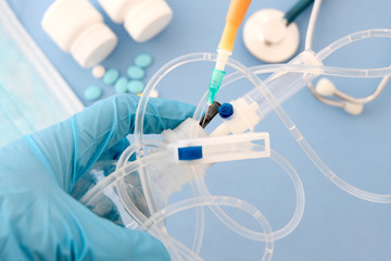 Hands in blue gloves hold the system. Top view of the doctor's Desk. Blurred stethoscope, pills, mask, blue background.Concept treatment of patients, treatment room.