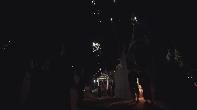Low angle pan down showing fireworks going off into the sky in Myanmar with silhouetted people