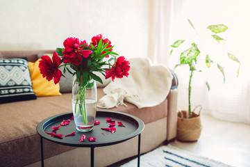 Interior of living room decorated with flowers, plants and carpet. Cozy couch with cushions and table
