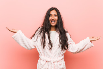 Young indian woman wearing pajama makes scale with arms, feels happy and confident.