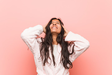 Young indian woman wearing pajama laughs joyfully keeping hands on head. Happiness concept.