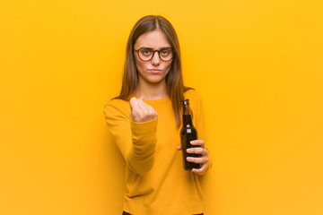 Young pretty caucasian woman showing fist to front, angry expression. She is holding a beer.