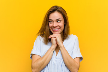 Young pretty young woman keeps hands under chin, is looking happily aside.