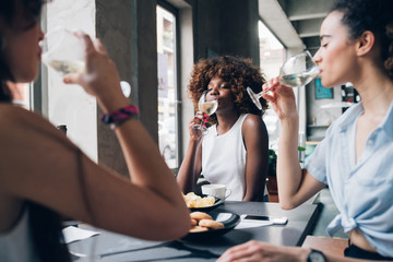 young multiracial women sitting in modern restaurant drinking together wine