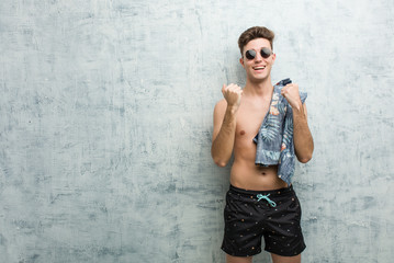 Fototapeta na wymiar Young caucasian man wearing a swimsuit cheering carefree and excited. Victory concept.