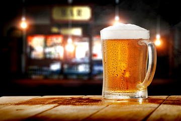 Cold fresh beer in glass on wooden table and free space for your decoration. Blurred bar interior 