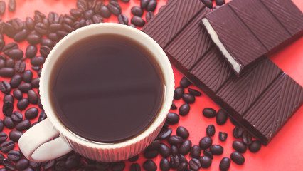 Coffee cup, coffee beans and chocolate on red background.