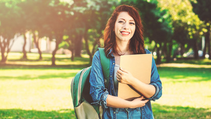 Female student outdoors holding notebook and smiling