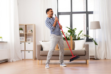 cleaning, housework and housekeeping concept - indian man with broom sweeping floor and singing at...