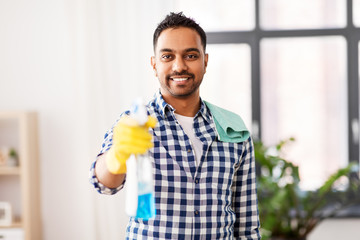 cleaning, housework and housekeeping concept - smiling indian man with detergent and rag on shoulder at home