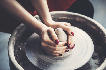 Work at potter wheel in apron. Hands of young woman with clay. Top view