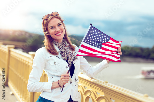 Happy young woman holding USA flag outdoors, 4th July