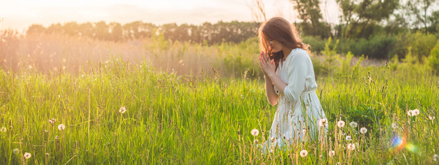 Girl closed her eyes, praying in a field during beautiful sunset. Hands folded in prayer concept...