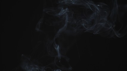 Thin trickle of gray smoke slowly rising graceful twists up on black background. Black and white smoke blowing from bottom to top. Closeup