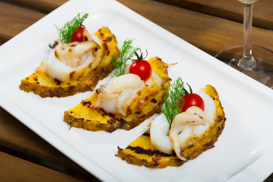 Photography of plate with sepia fried on a grill with pineapple, cherry tomatoes and sauce Chile