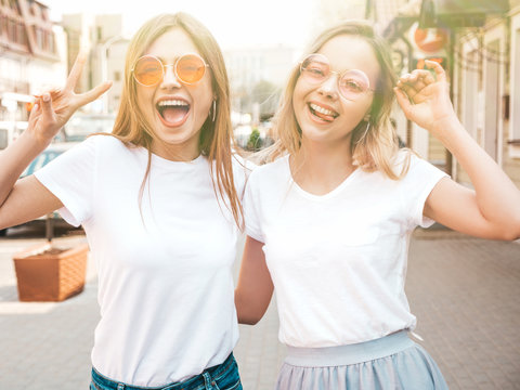 Portrait of two young beautiful blond smiling hipster girls in trendy summer white t-shirt clothes. Sexy carefree women posing on street background. Positive models having fun.Shows peace sign