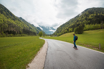 Man ride longboard skate board in Logar Valley between snowy mountains forest in Spring vacation boy, Logarska dolina, Slovenia&nbsp;