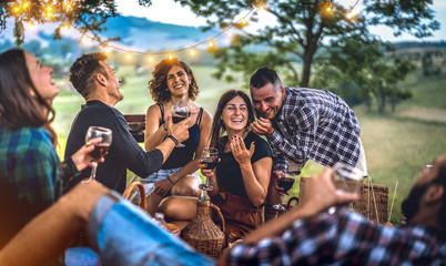 Young friends having fun at vineyard after sunset - Happy people millennial camping at open air pic nic under bulb lights - Youth friendship concept with guys and girls drinking wine at barbeque party - obrazy, fototapety, plakaty