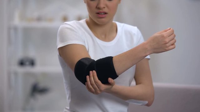 Woman applying elbow padded orthosis, feels pain after sport injury, orthopedics