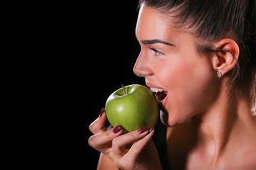 young fitness model eat an apple on black background