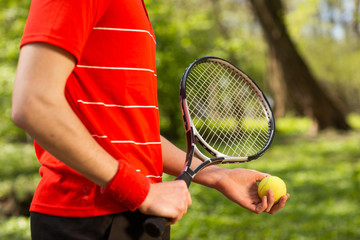 Close up of men's hands hold a tennis racket and ball on the green background. Sport concept