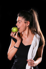 young fitness model eat an apple on black background