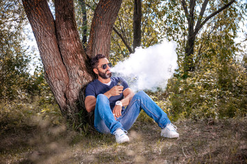 Naklejka na ściany i meble Confident vaper blows up a couple an vape on the forest floor. Electronic cigarette concept.