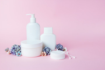 Obraz na płótnie Canvas White jars of cosmetics with flowers on a pink background. Bath accessories. Face and body care concept