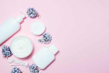 White jars of cosmetics with flowers on a pink background. Bath accessories. Face and body care concept. Top view