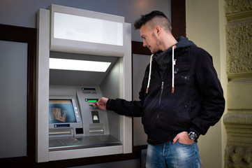 young man insert credit card to atm at night