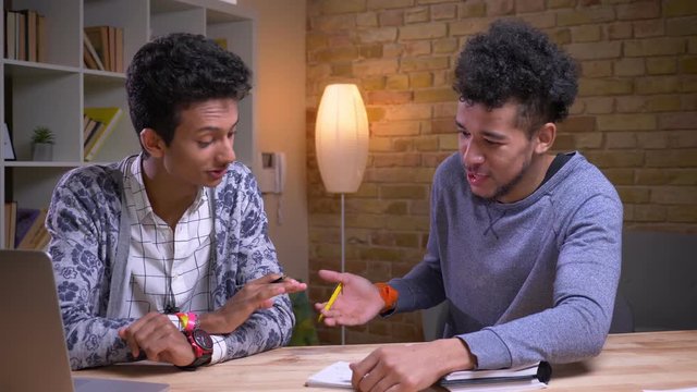 Closeup shoot of african american and indian male students learning together. Two friends playing a tic tac toe and arguing