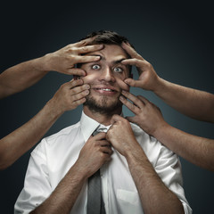 A male model surrounded by hands like his own thoughts on dark background. A young man doubts, can't choose the right decision, losing sleep. Concept of mental problems, troubles in work, indecision.