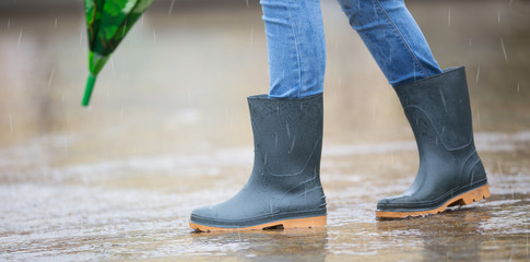 Girl feet in rubber boots with umbrella under rain in puddle