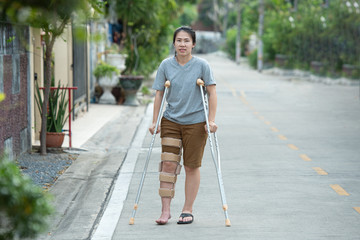 Disabled woman with crutches or walking stick or knee support standing with full lenght body.