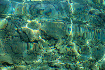 Top view of blue, green and turquoise colors of water, surface of sea on rocks and bottom. Reflection of sun beams in water, shallow soil, shoal of ocean. Sea texture, background, pattern, wallpaper.