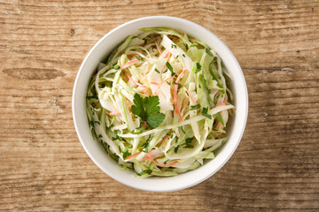 Coleslaw salad in white bowl on wooden table. Top view