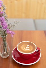 Red hot coffee cup with latte art on wood table and flowers vase decoration
