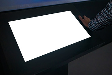 Man looking at white blank interactive touchscreen display of electronic multimedia kiosk in dark...
